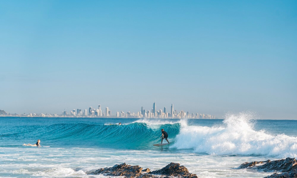 Man rides the surf break at Currumbin Rocks with Gold Coast skyline in the background