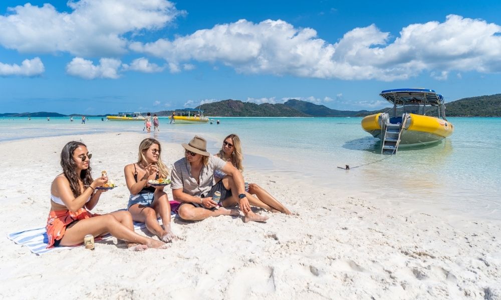Group of friends sitting on Whitehaven Beach eating lunch