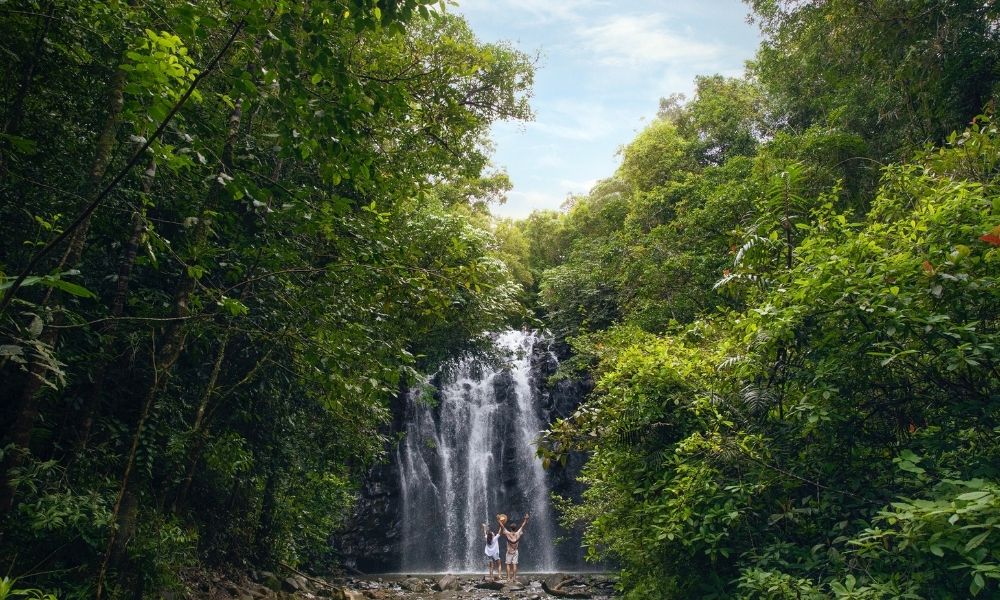 Couple standing at the base of the Elinjaa Waterfalls in Atherton Tablelands