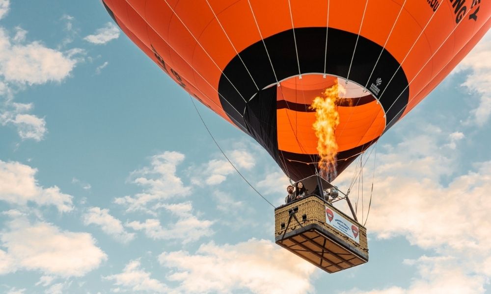 An orange hot air balloon with a ball of fire lifts off the ground